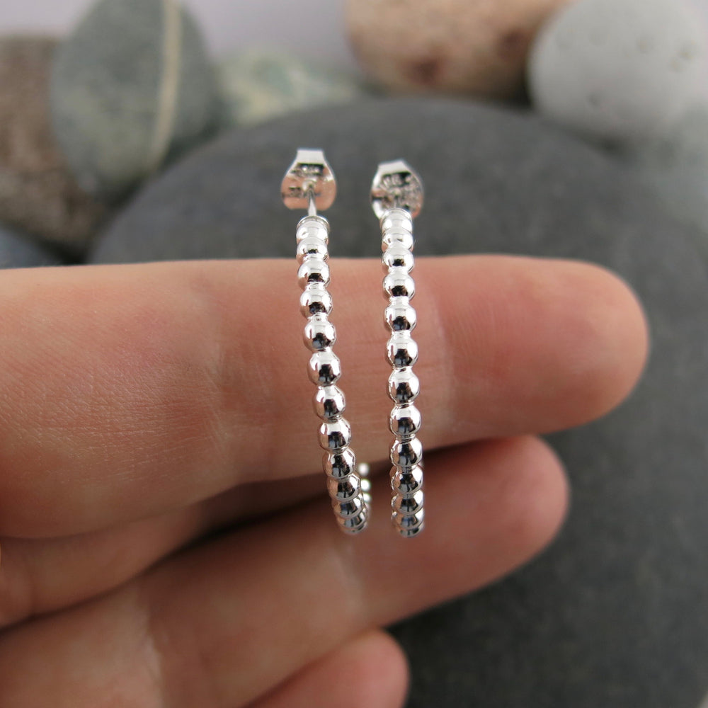 Beaded sterling silver open hoop studs displayed on a hand by Mikel Grant Jewellery. Artisan made on the Sunshine Coast of BC.
