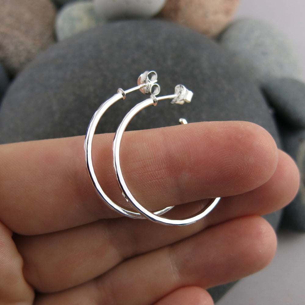 Hammer textured sterling silver open hoop stud earrings displayed on a hand  by Mikel Grant Jewellery. Artisan made on the Sunshine Coast of BC.