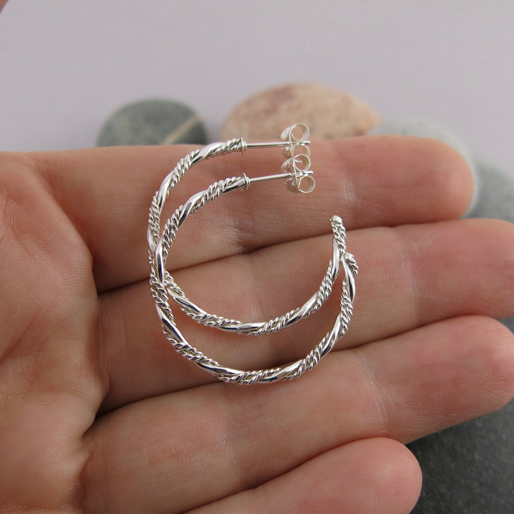 Sterling silver ornate twist open hoop stud earrings displayed on a hand by Mikel Grant Jewellery. Artisan made on the Sunshine Coast of BC.