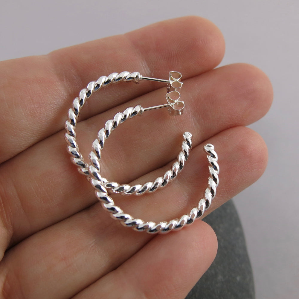 Twisted sterling silver open hoop studs displayed on a hand by Mikel Grant Jewellery. Modern, comfortable, artisan made.