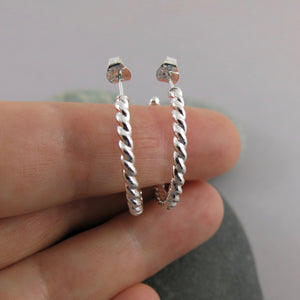 Twisted sterling silver open hoop studs displayed on a hand by Mikel Grant Jewellery. Modern, comfortable, artisan made.